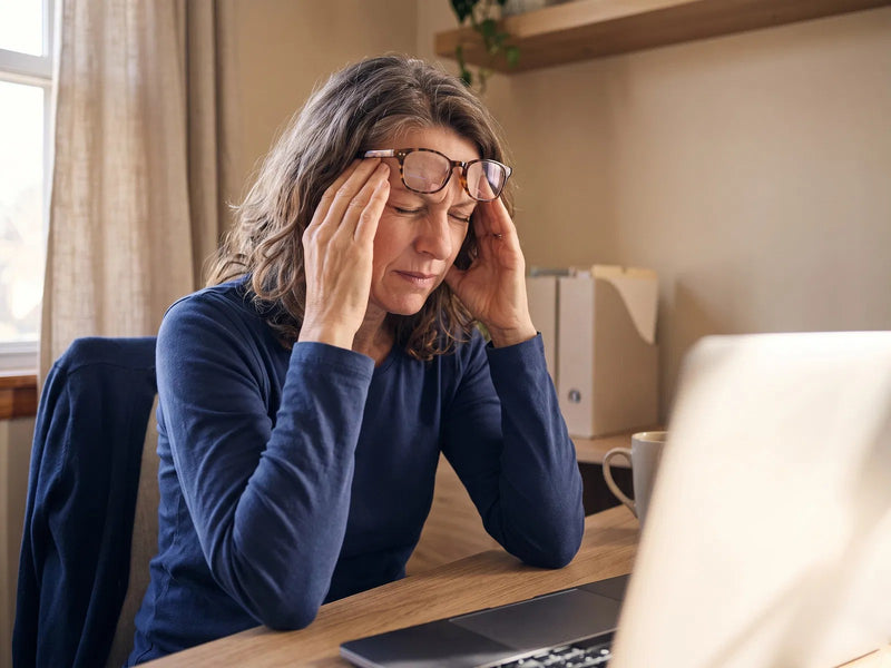 A woman at her laptop holding her head, struggling to focus